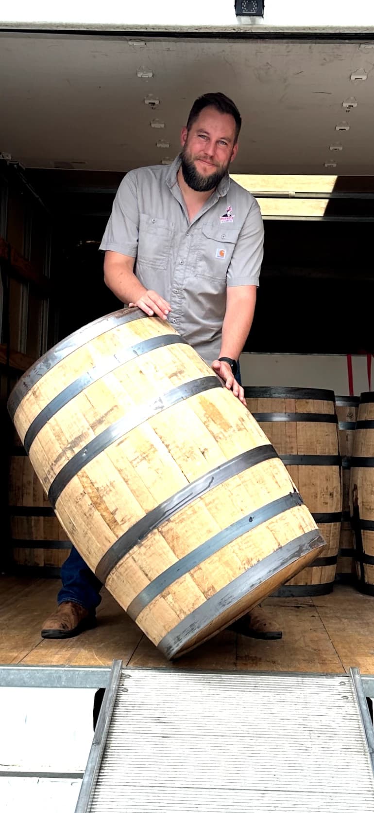 Will Correll in the back of a box truck, tipping a wooden barrel toward the ramp.